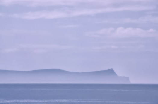 The constant wind creates a mist over the ocean.